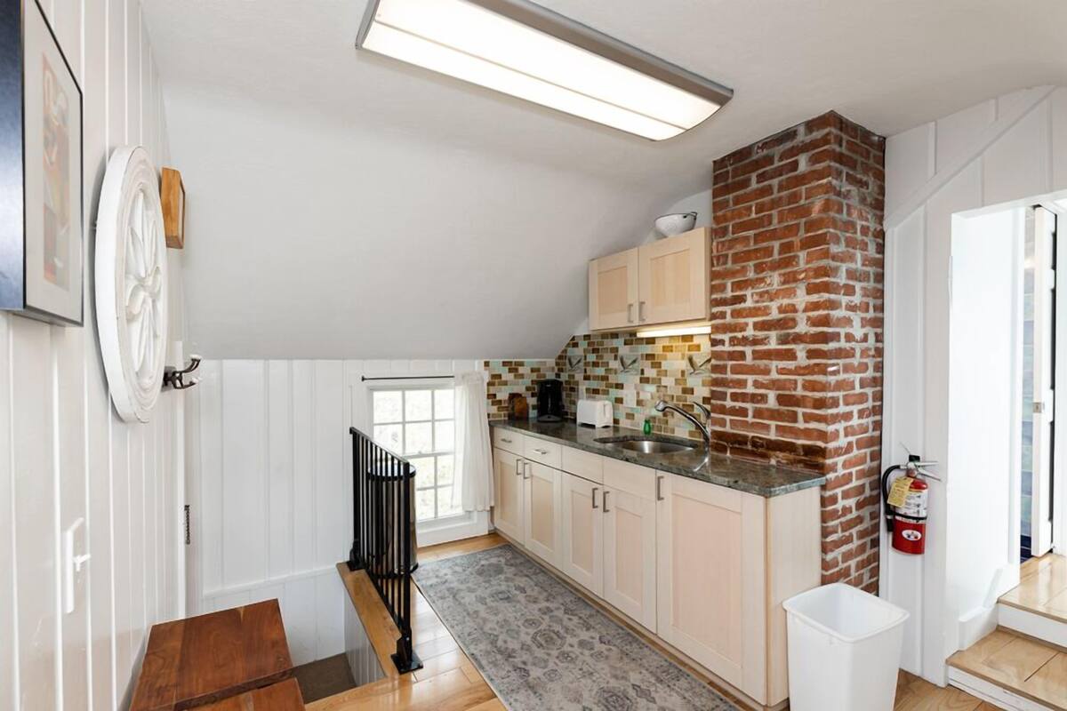 A kitchen with white cabinets, a brick accent wall, a window, and a fire extinguisher.