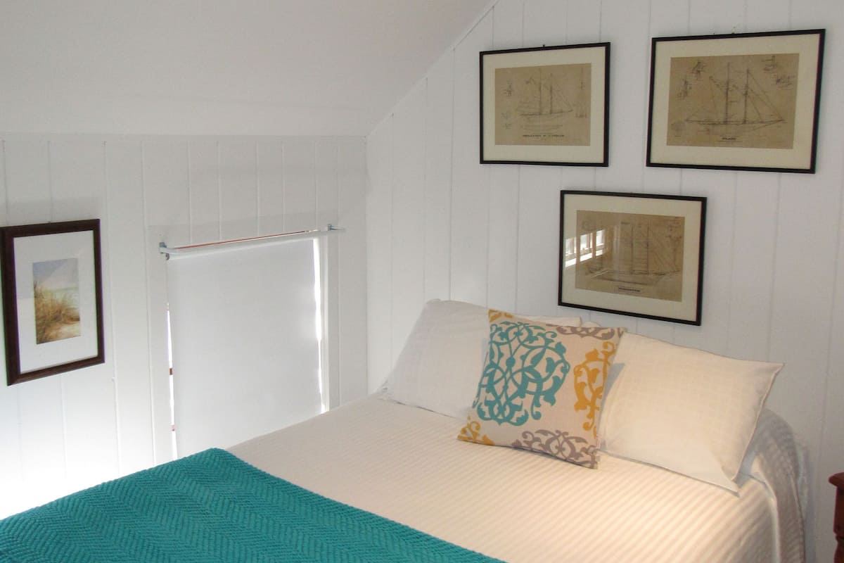 A bedroom with a bed, a window, and three framed pictures on the wall.