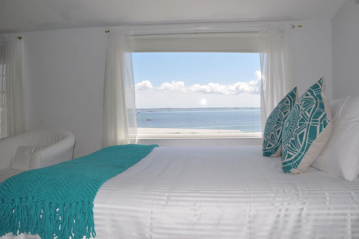A bedroom with a bed, a view of the sea, and a white wall.