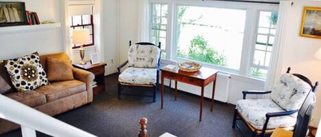 A cozy living room with a brown leather sofa, two patterned armchairs, a wooden coffee table, and a white radiator.