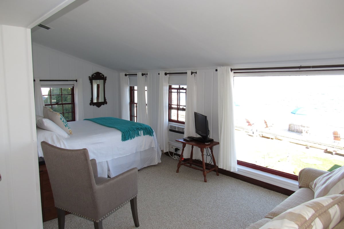 A hotel room with a bed, a chair, a TV on a small table, and a large window with a view of the outside.