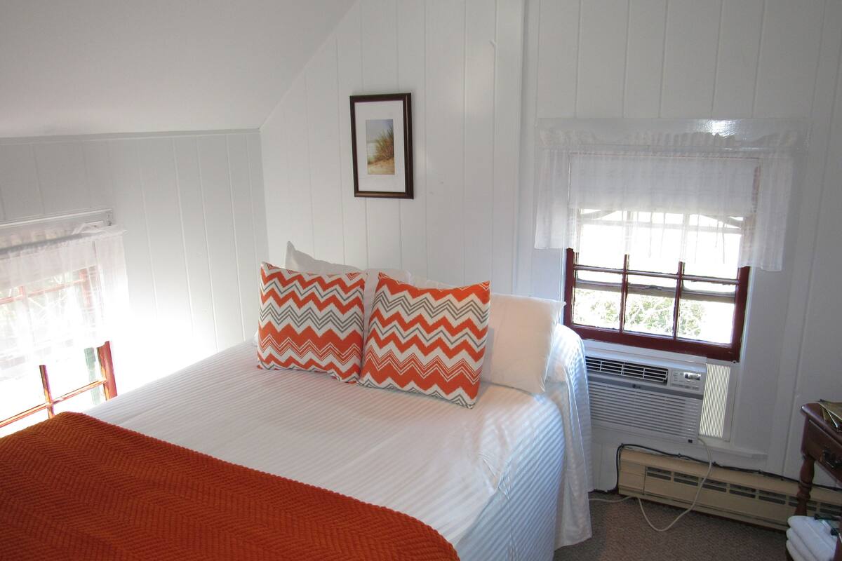 A bedroom with a bed, a window with curtains, a radiator, and a picture on the wall.