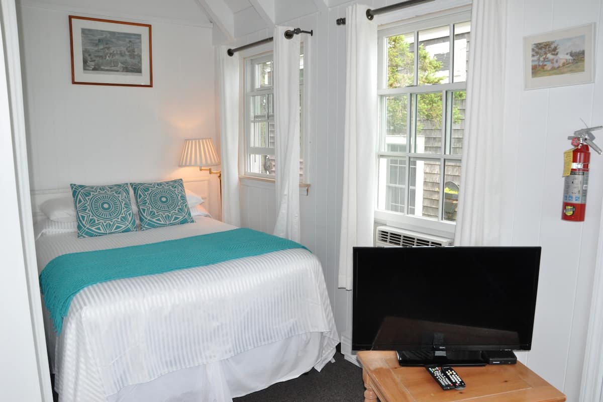A hotel room with a bed, a TV, a remote control, and a fire extinguisher.