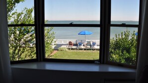 Blick aus einem Fenster auf einen Poolbereich mit Liegestühlen und einem blauen Sonnenschirm.