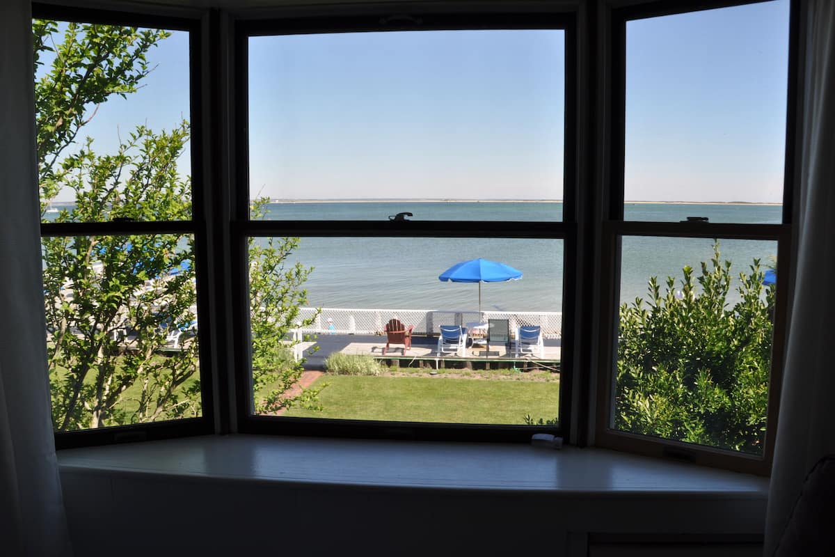 A view from a window overlooking a pool area with lounge chairs and a blue umbrella.