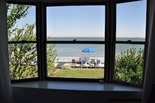 A view from a window overlooking a pool area with lounge chairs and a blue umbrella.