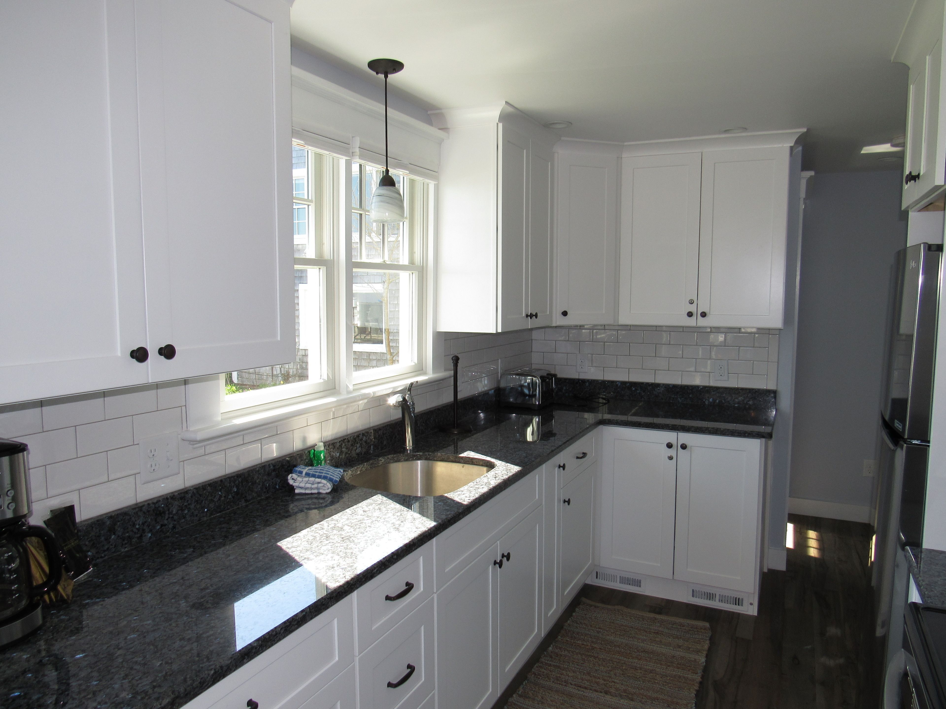 A kitchen with white cabinets, a granite countertop, a stainless steel sink, and a refrigerator.