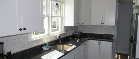 A kitchen with white cabinets, a granite countertop, a stainless steel sink, and a refrigerator.