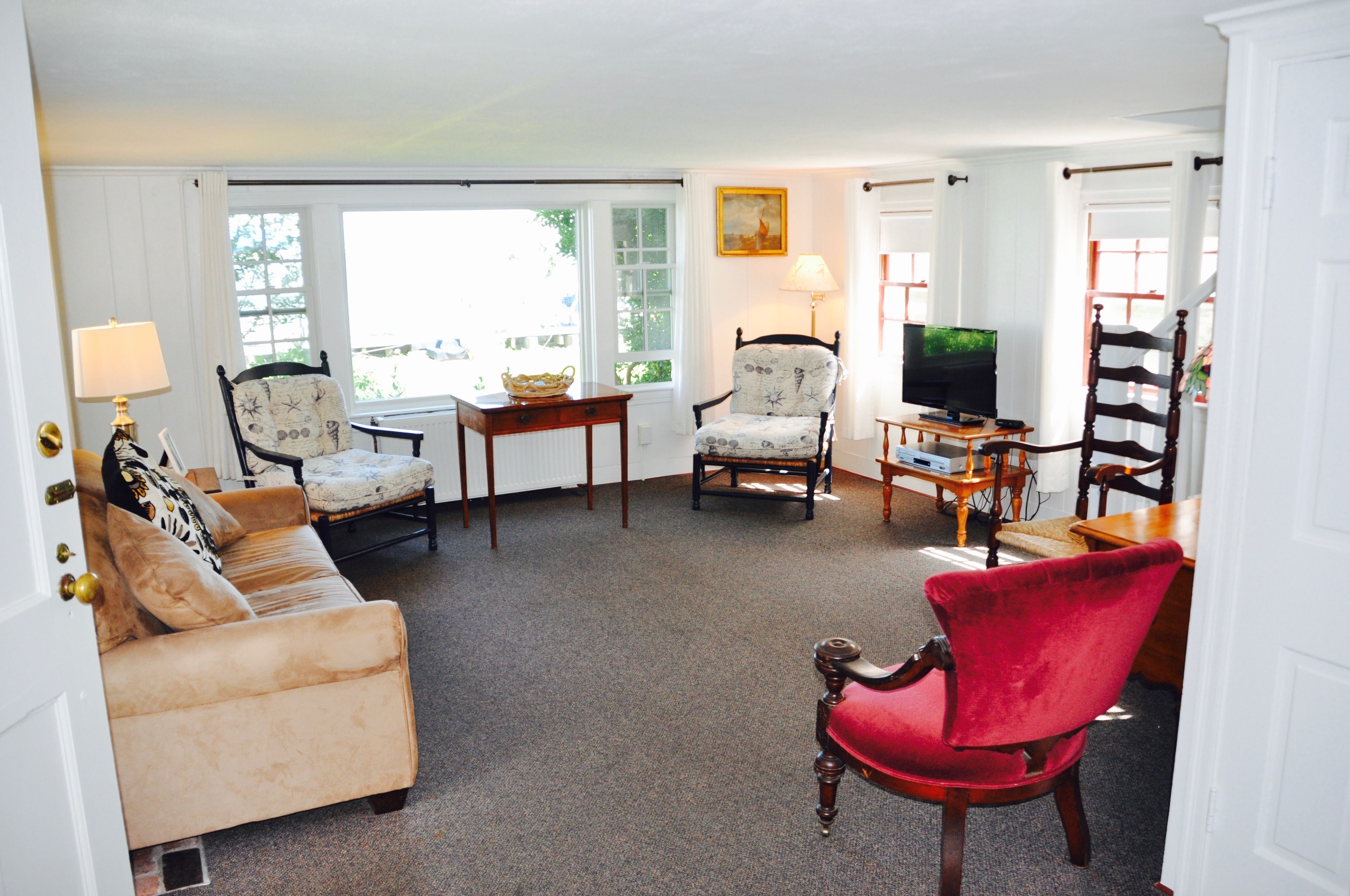 A living room with a beige sofa, a red chair, a wooden coffee table, and a television.