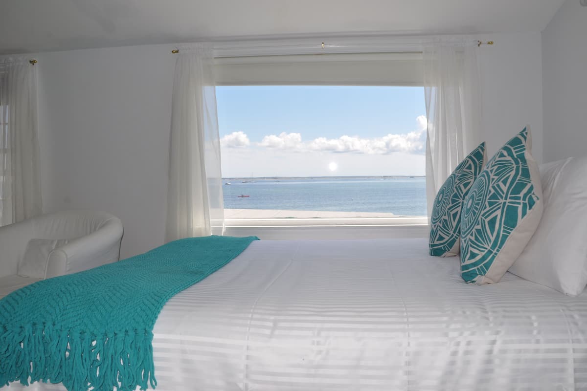 A hotel room with a bed, a view of the sea, and a white chair.
