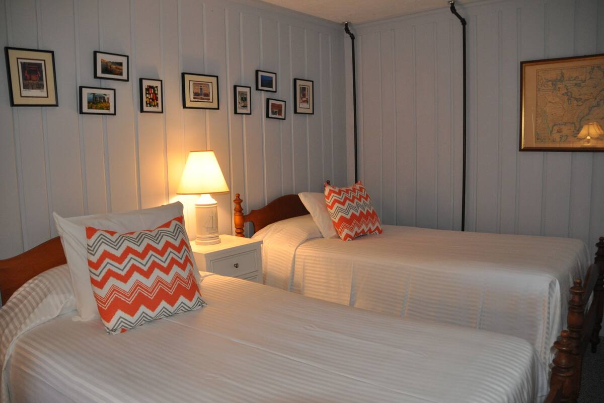 A hotel room with two beds, a nightstand with a lamp, and framed pictures on the wall.