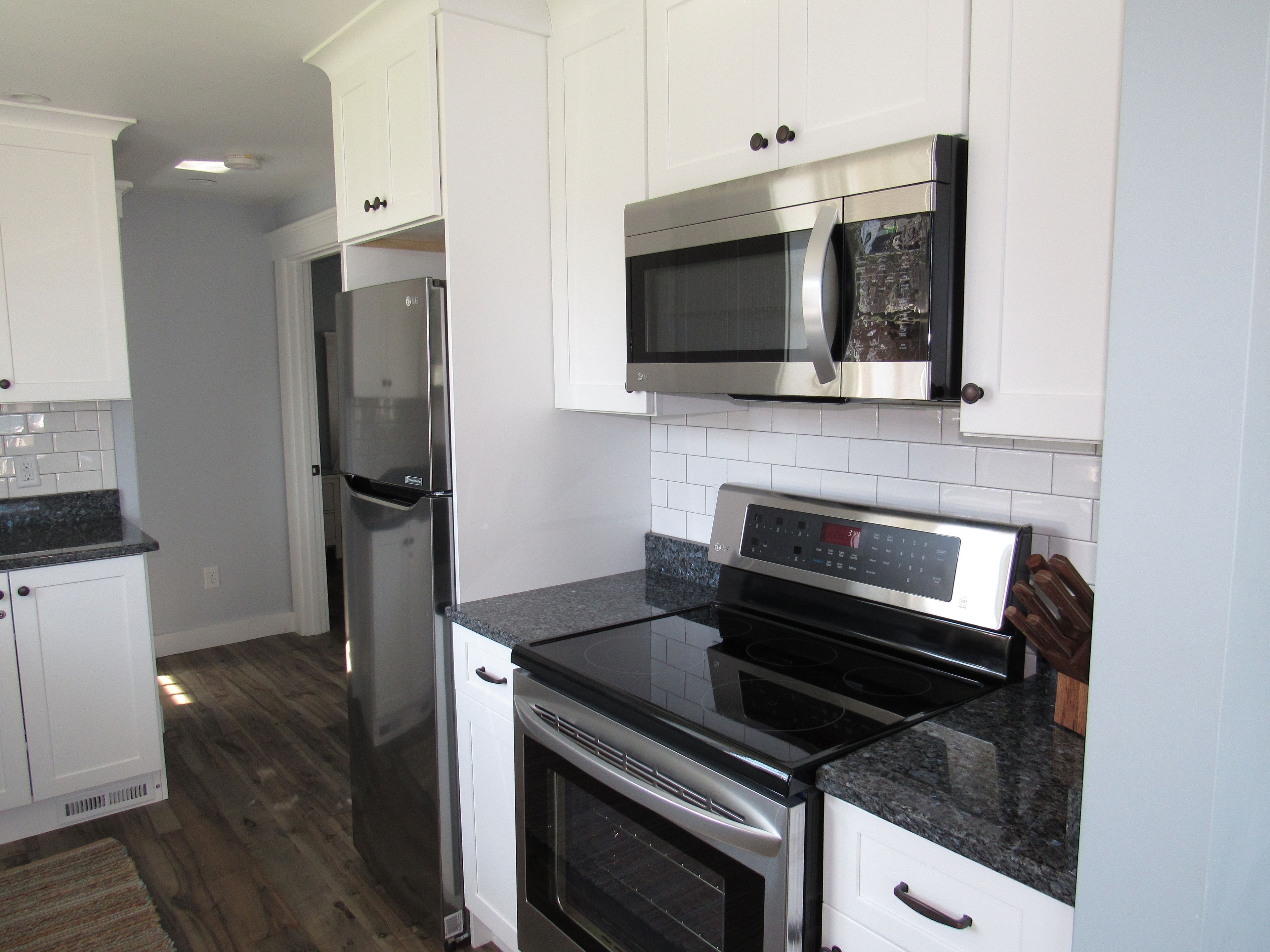A modern kitchen with white cabinets, a stainless steel refrigerator, a microwave, and an oven.