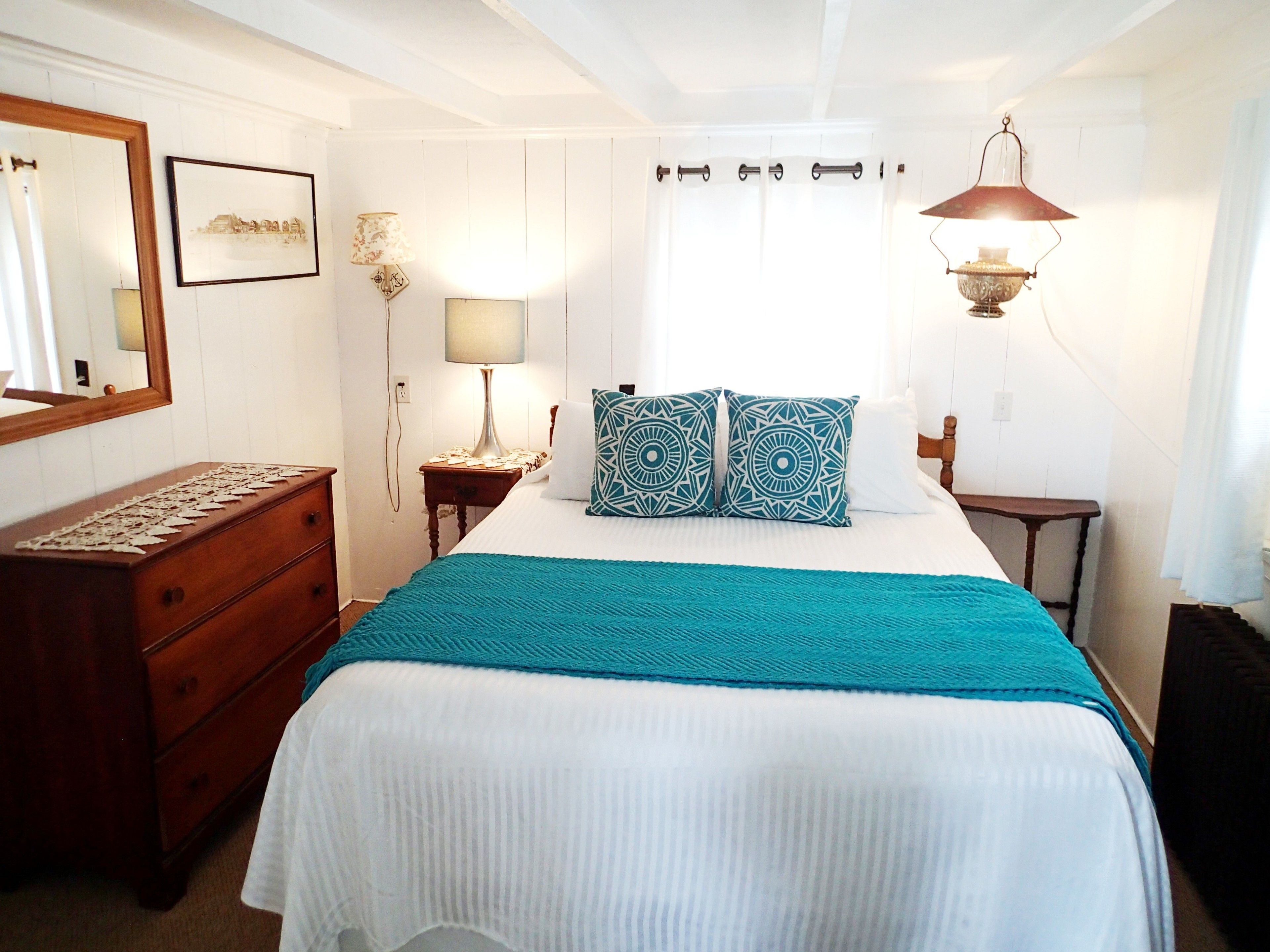 Une chambre à coucher comprenant un lit, une commode, une table de chevet, une lampe et un miroir.