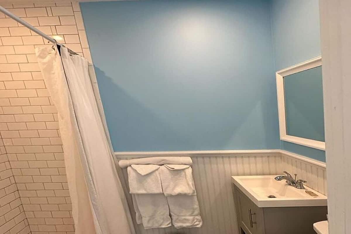A bathroom with a blue wall, white tiled floor, a white sink, and a shower curtain.