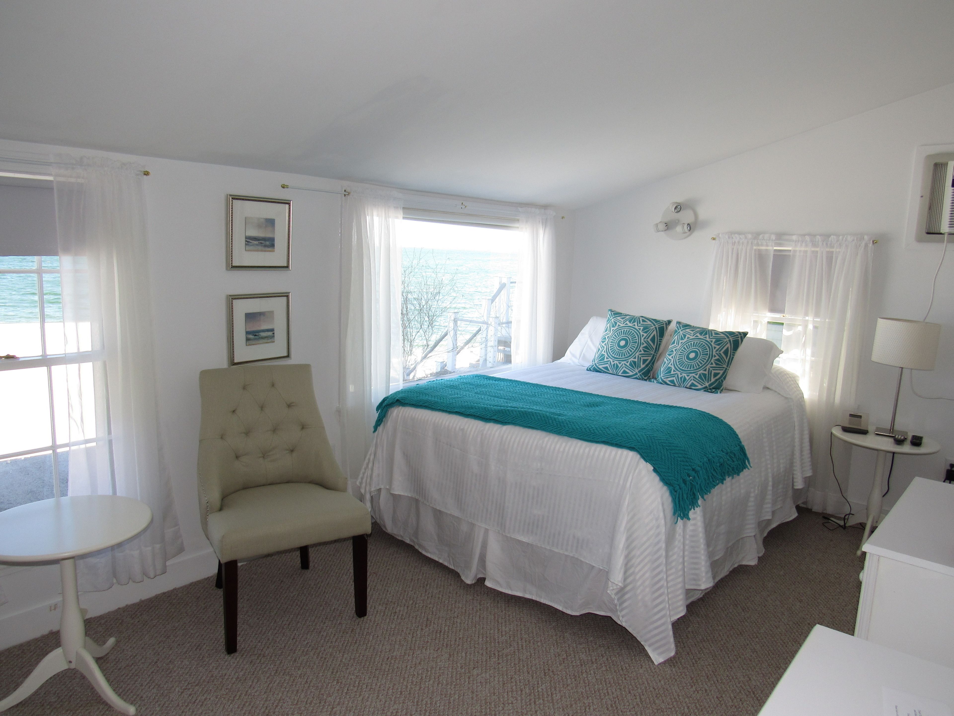 A hotel room with a bed, a chair, a small table, and a lamp.