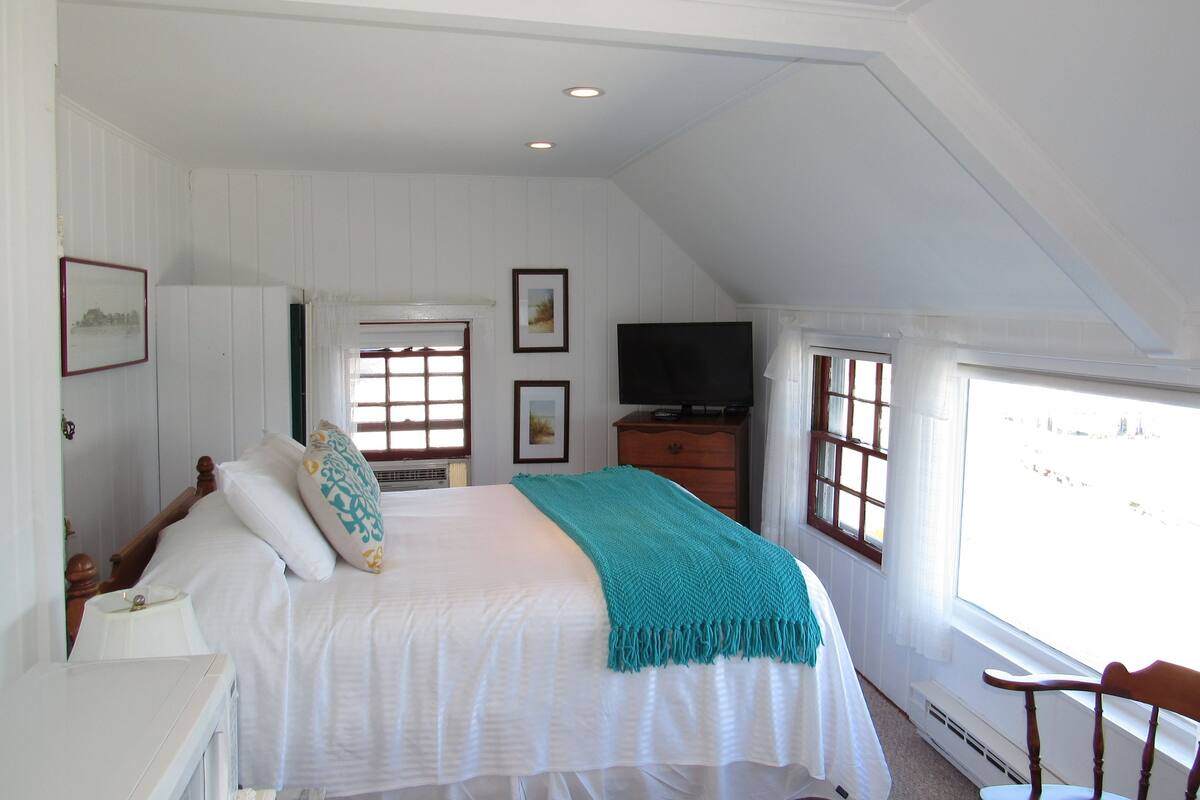 A bedroom with a bed, a television, a dresser, and a window with curtains.