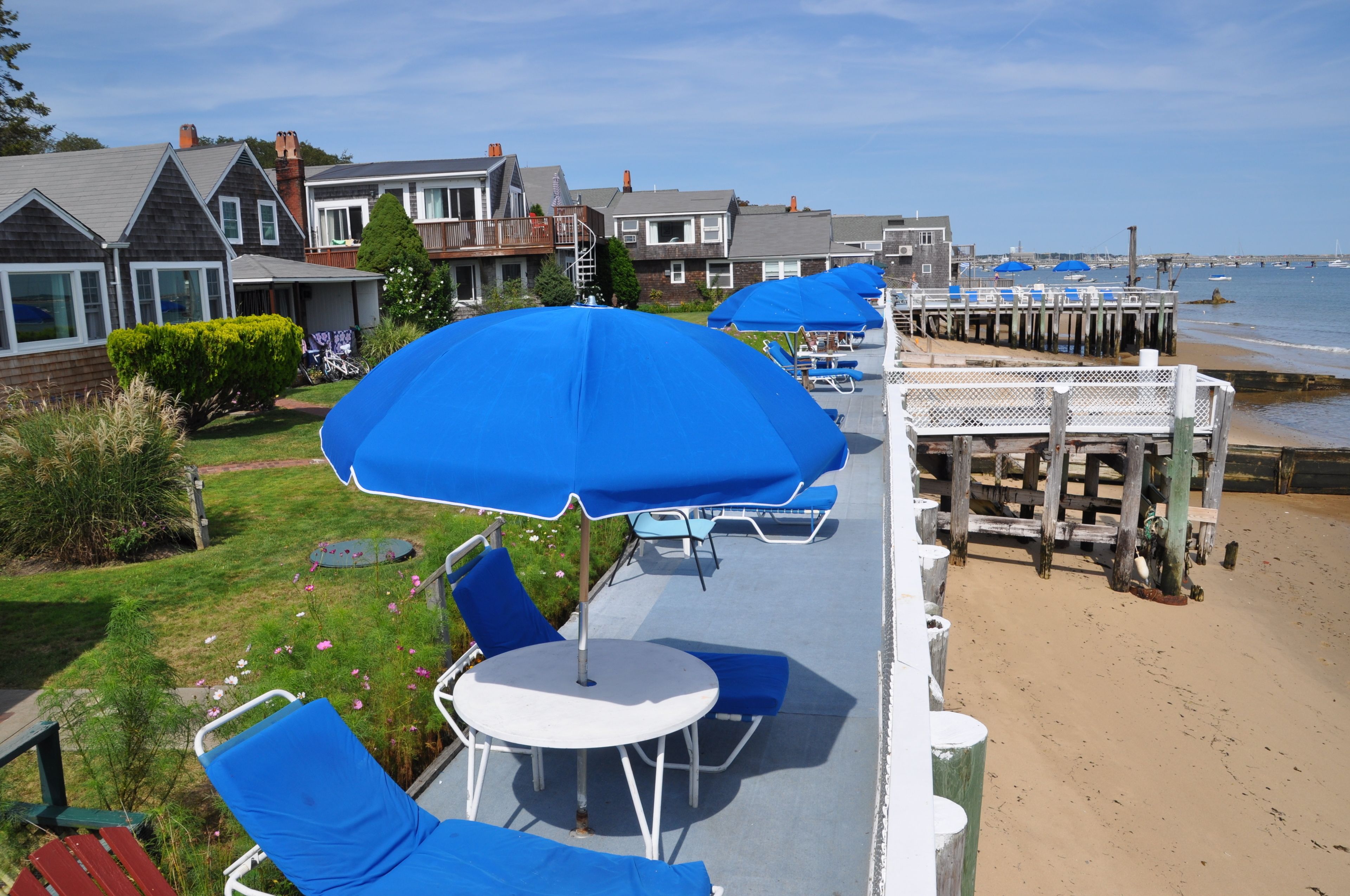 Une terrasse en bord de mer, agrémentée de parasols bleus, de chaises longues et offrant une vue sur l’océan.