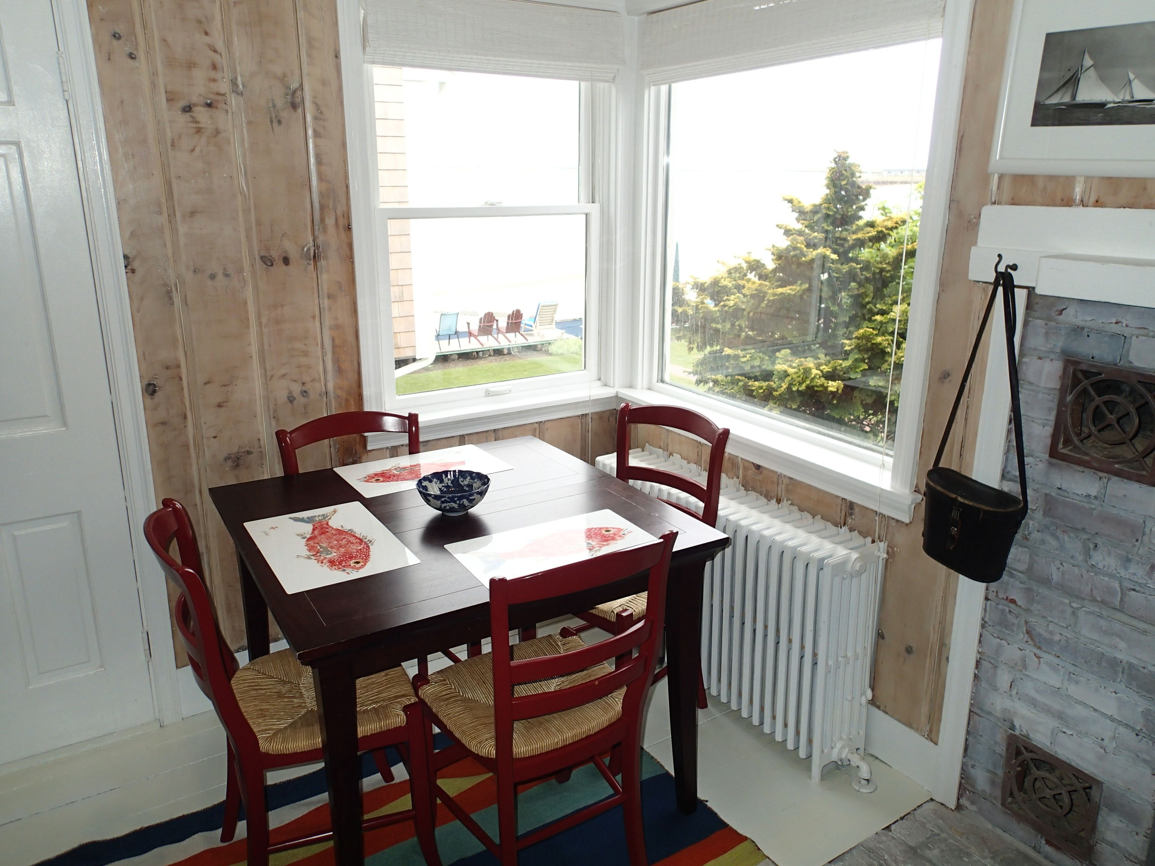 Un comedor con una mesa de madera y cuatro sillas, una ventana que ofrece vistas a un jardín y un radiador blanco.