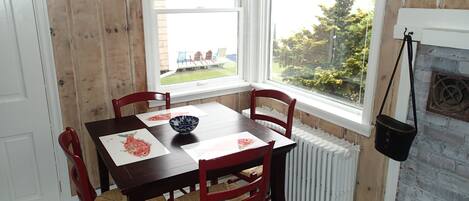 Un comedor con una mesa de madera y cuatro sillas, una ventana que ofrece vistas a un jardín y un radiador blanco.