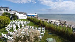 A coastal venue with white chairs arranged for an event, a white tent, and a view of the sea. - The Masthead Resort (Provincetown)
