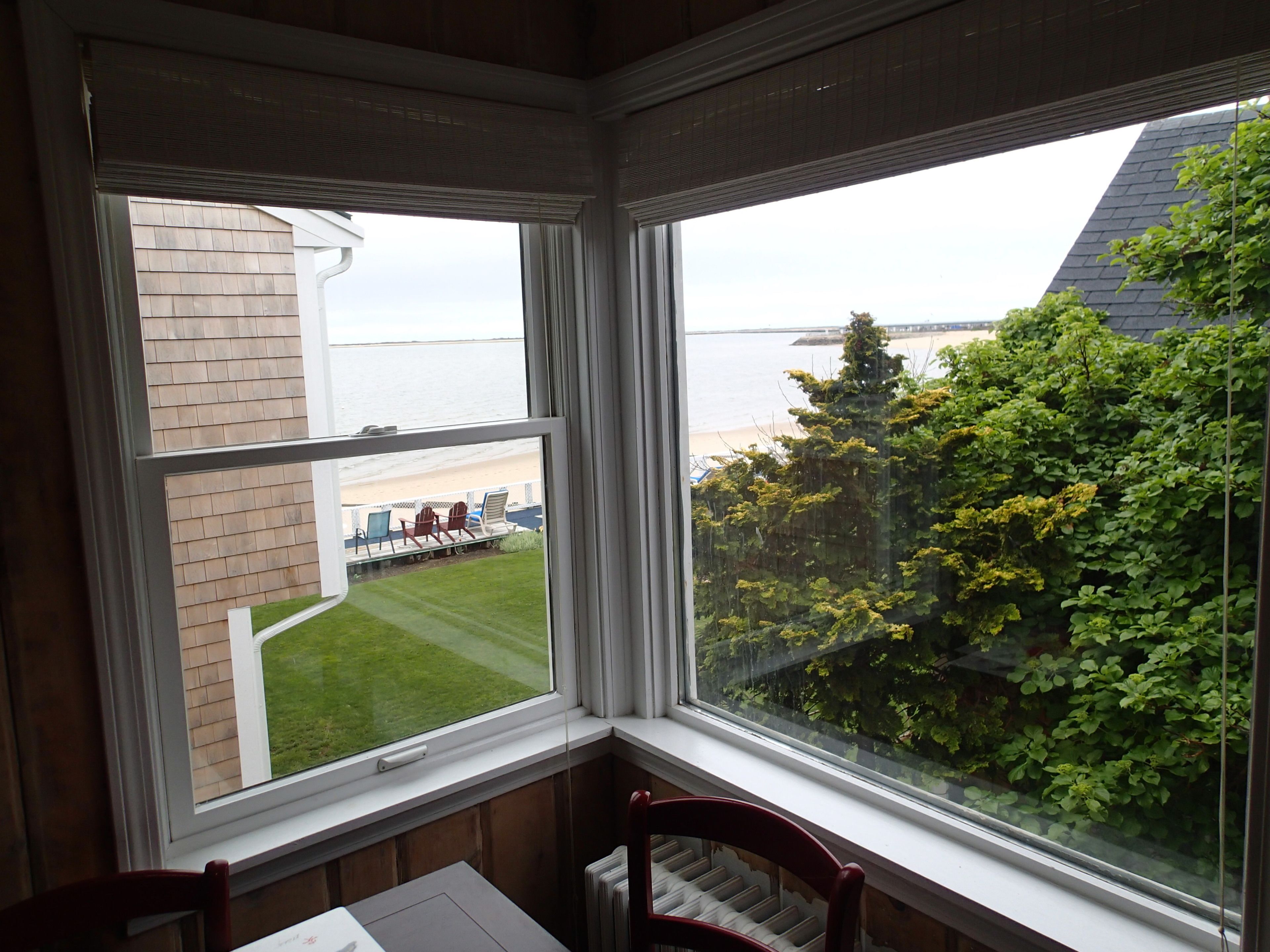 A room with a large bay window overlooking a grassy yard and a beach.