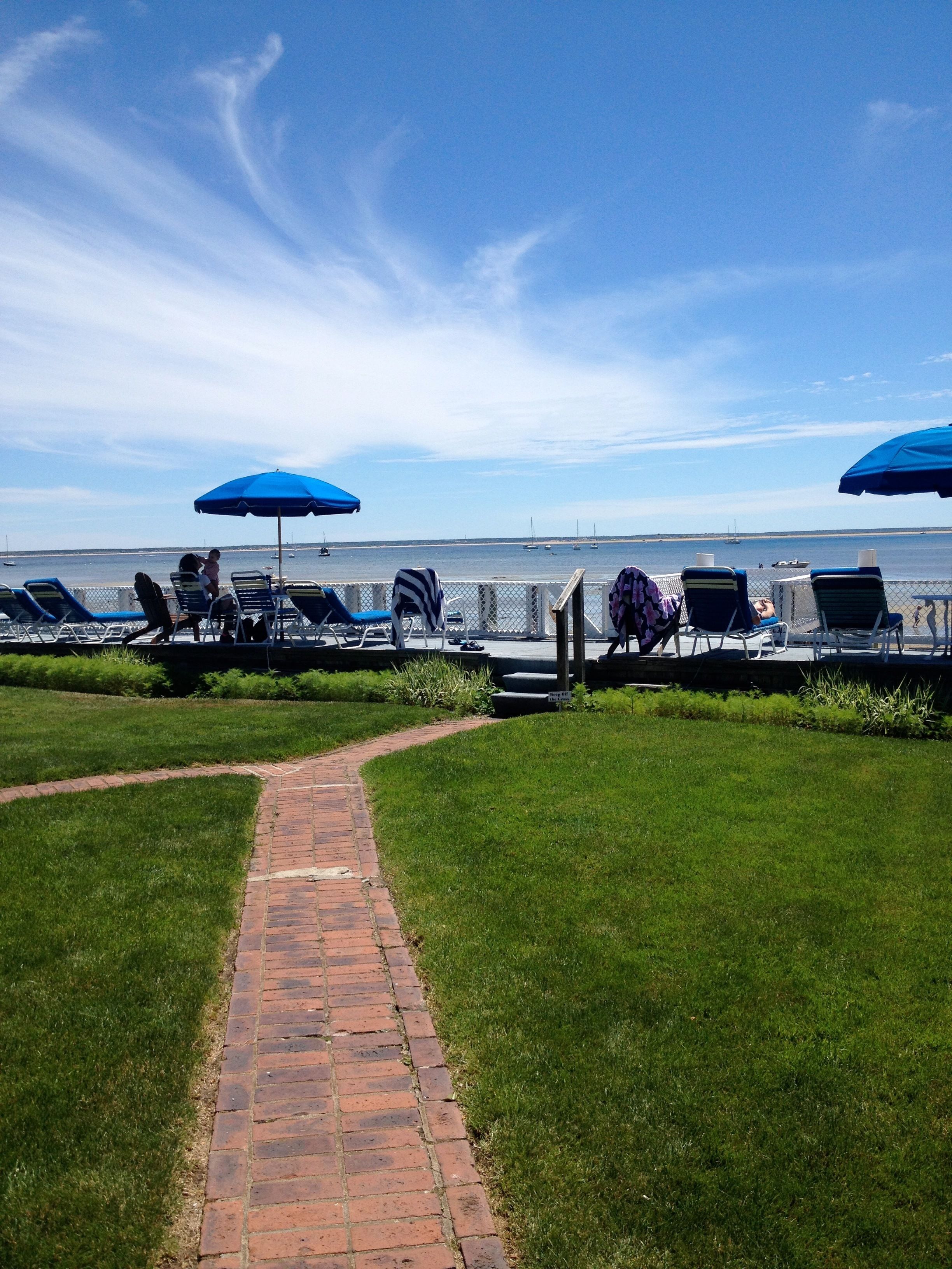 A pathway leading to a beachside lounge area with blue umbrellas and lounge chairs.