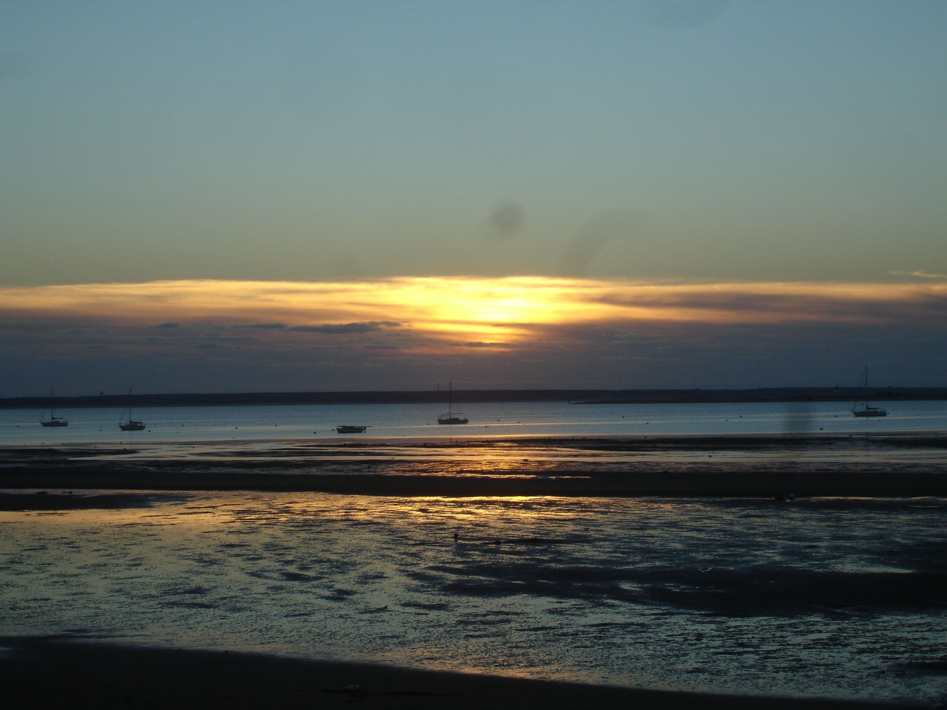 Een strand bij zonsondergang met boten op het water.