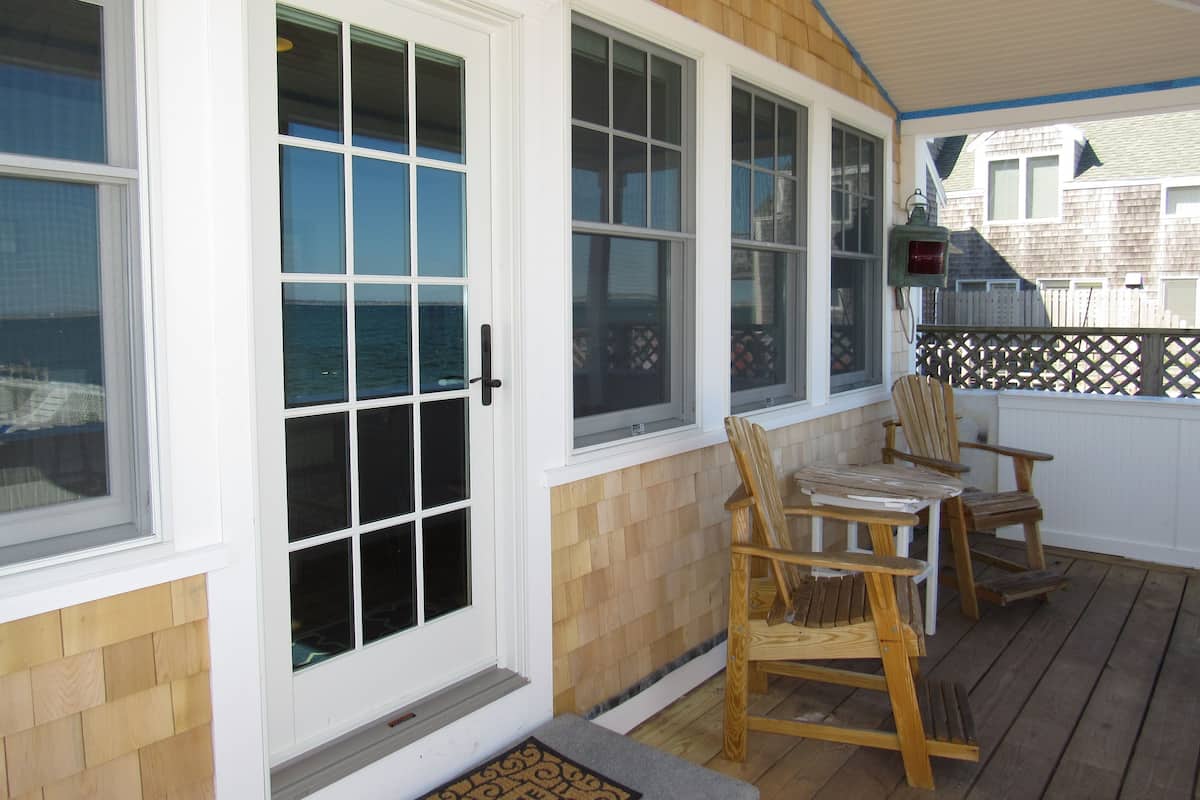 A covered porch with wooden flooring, white-framed windows, and two wooden chairs.