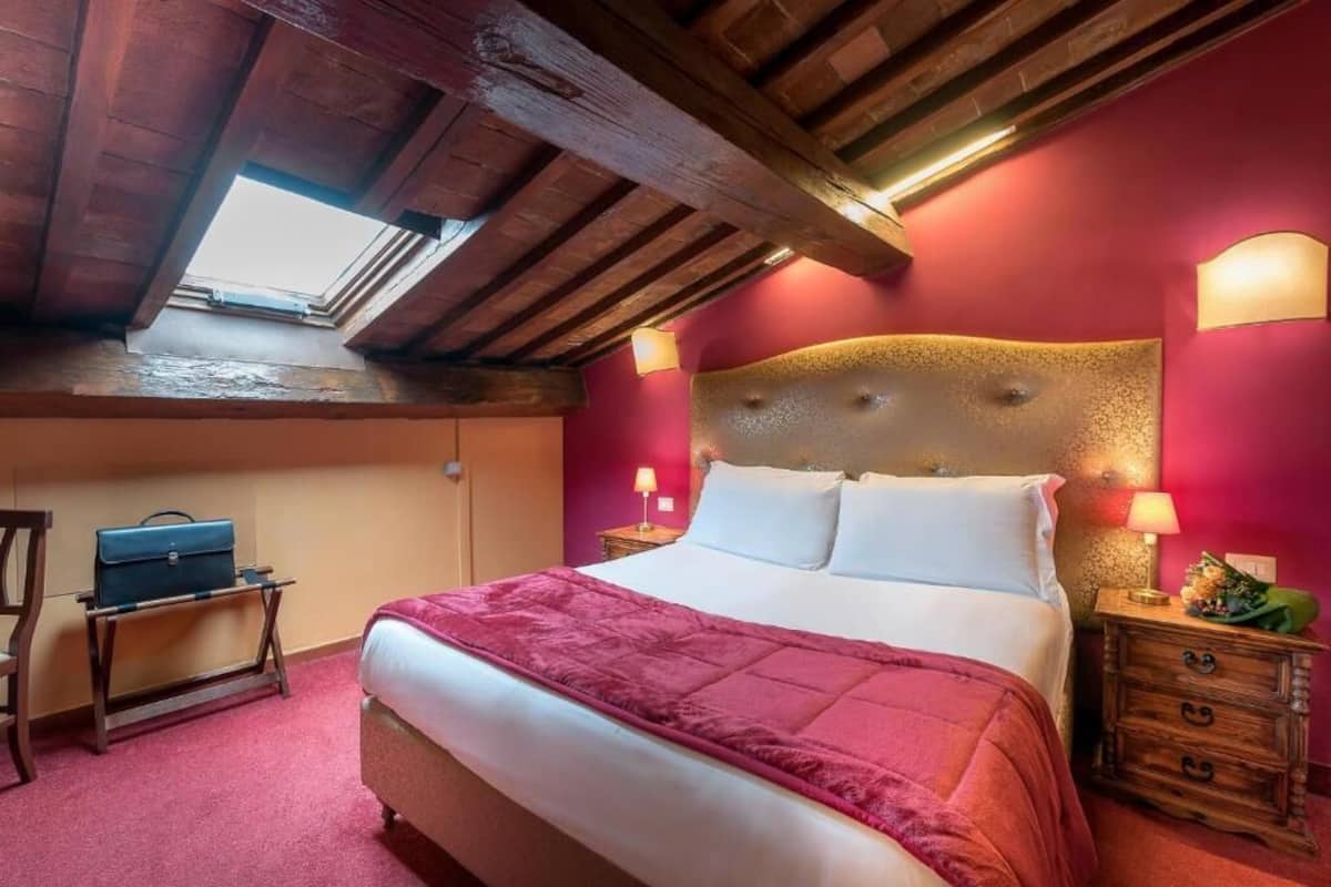 Un dormitorio con una cama grande, vigas de madera en el techo, un tragaluz y dos mesitas de noche con lámparas.