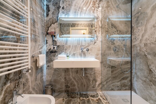 A modern bathroom with a marble wall, a glass-enclosed shower, a white sink, and a towel rack. - Hotel Ginori al DUOMO (Florence)
