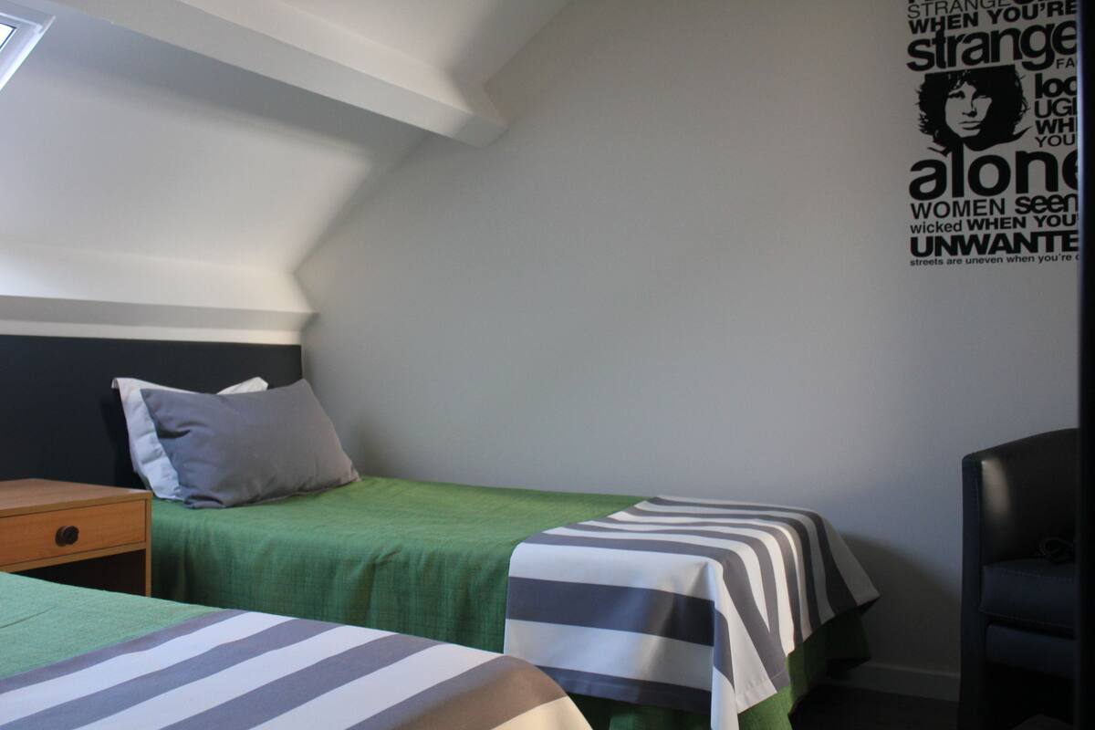 Un dormitorio con dos camas, una mesita de noche, una silla y una pared con un cartel.