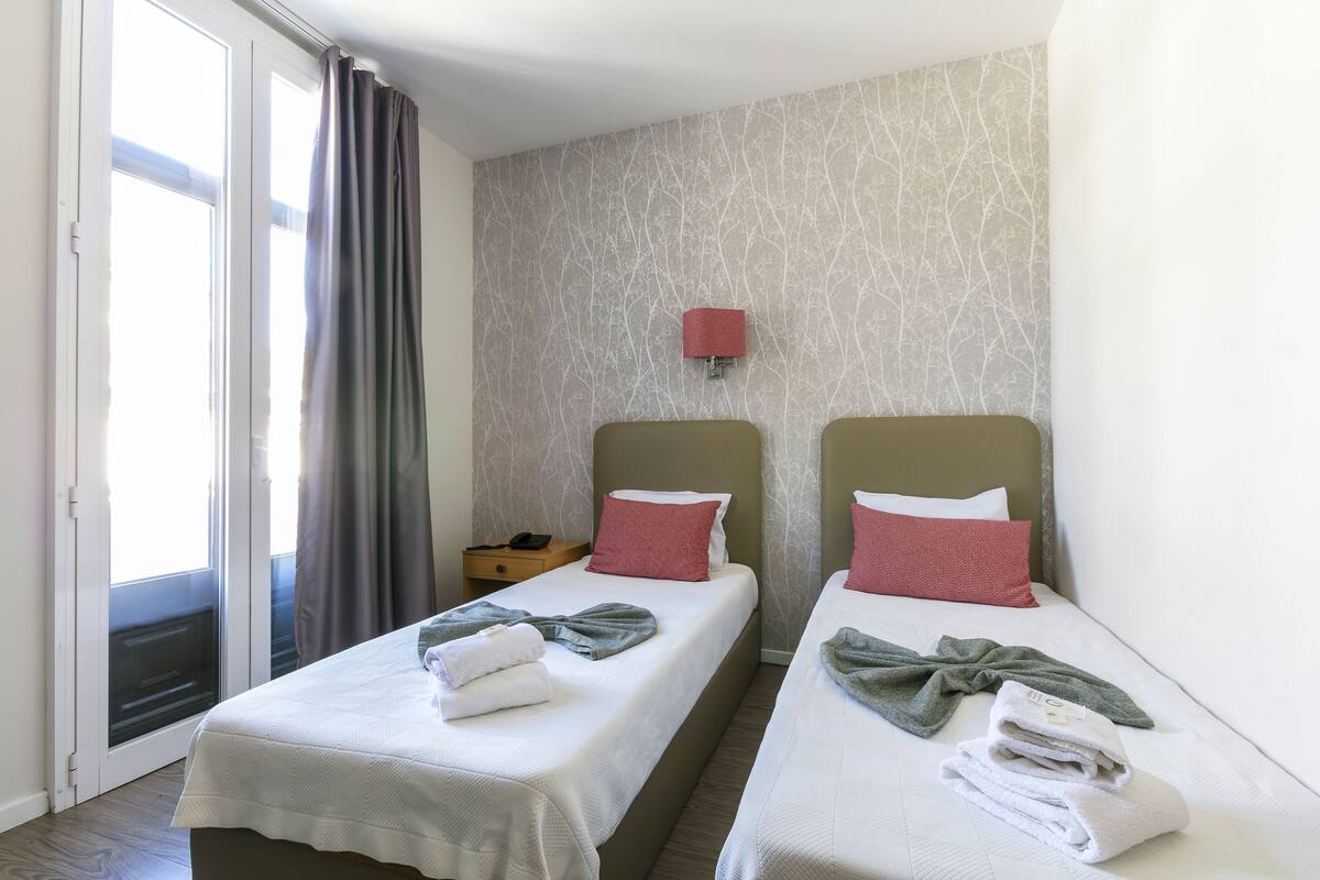 Habitación de hotel con dos camas, una mesita de noche, una lámpara roja y una puerta corrediza de cristal.