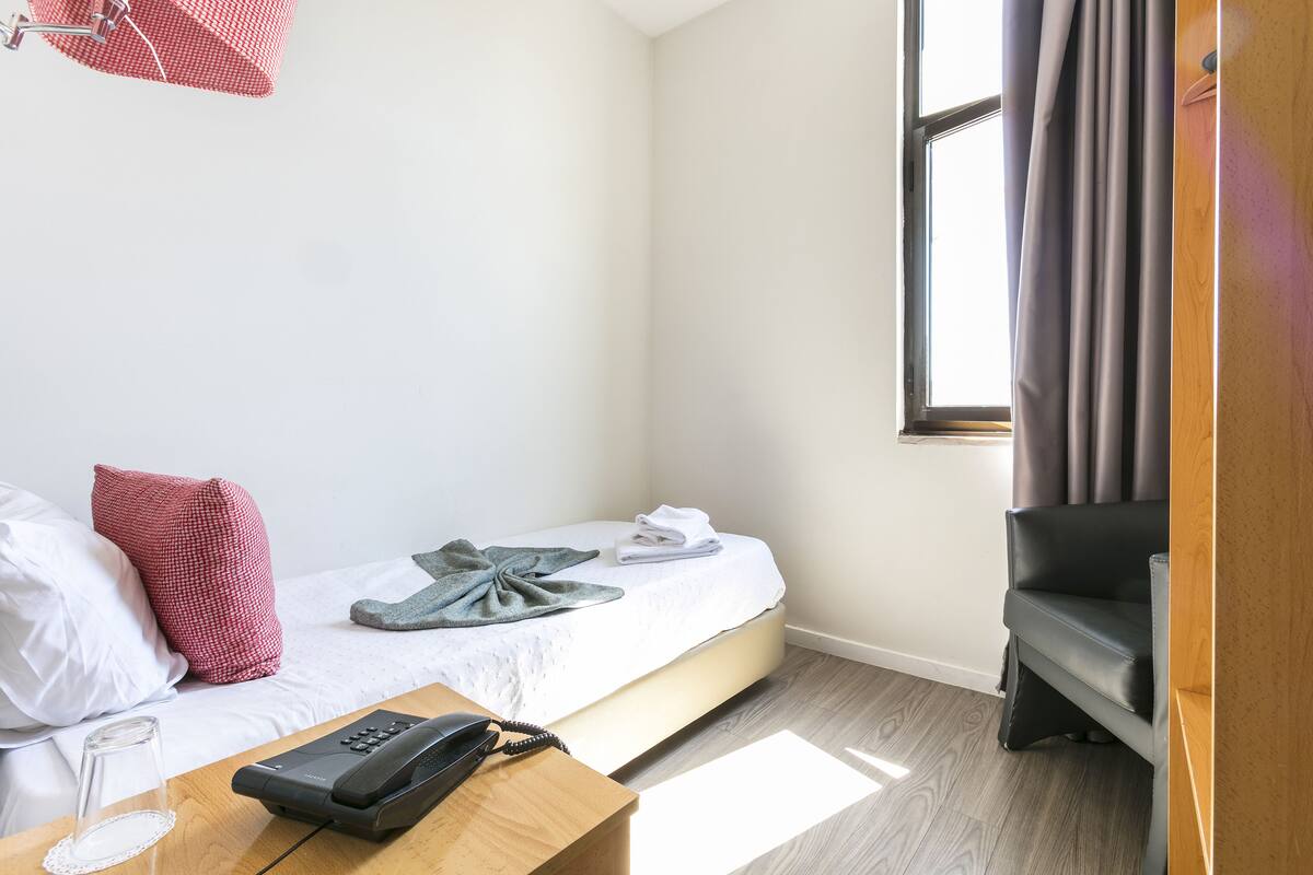 Habitación de hotel con cama, escritorio con teléfono, una silla y una ventana con cortinas.