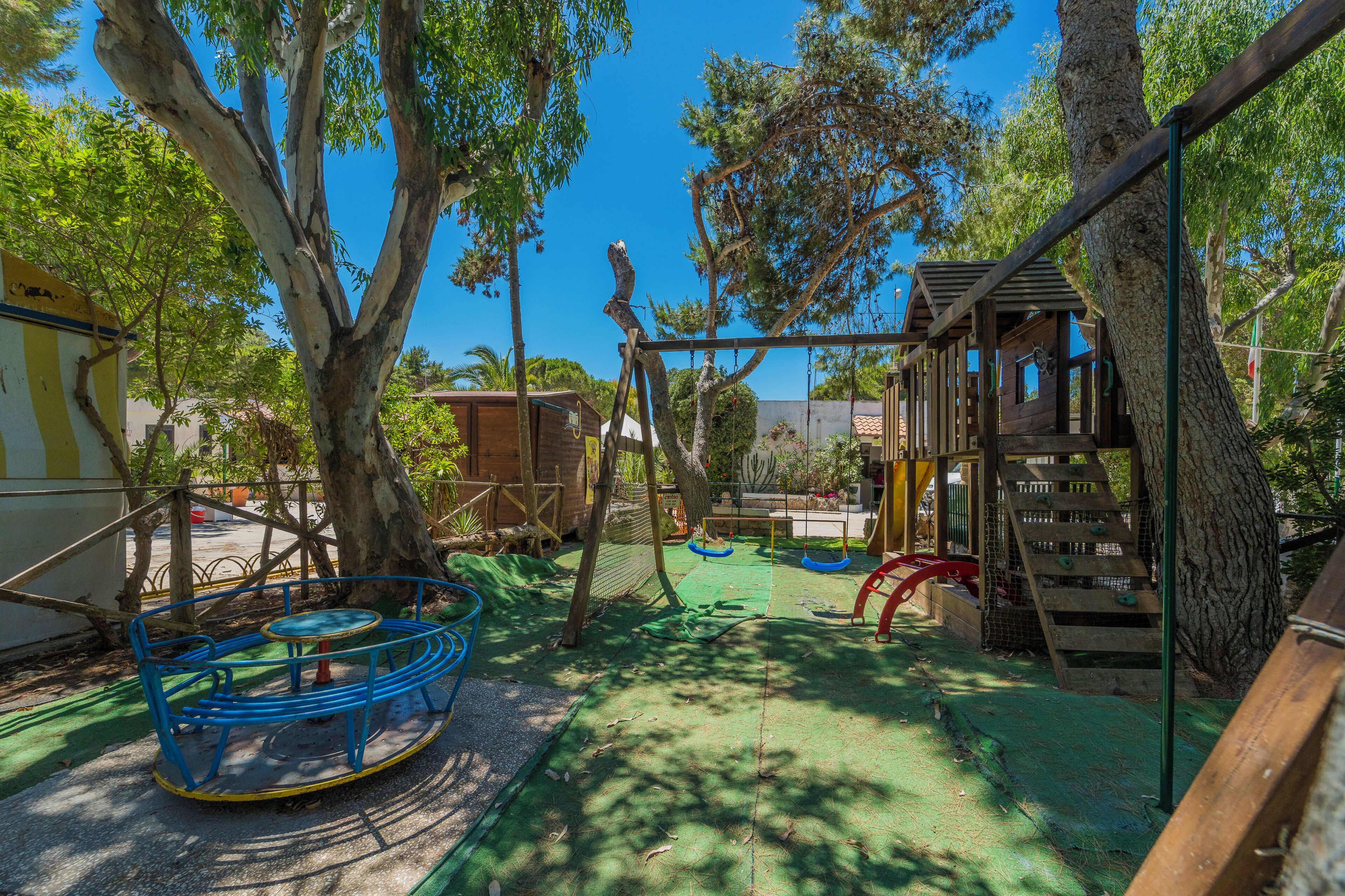A playground with swings, slides, and climbing structures surrounded by trees.