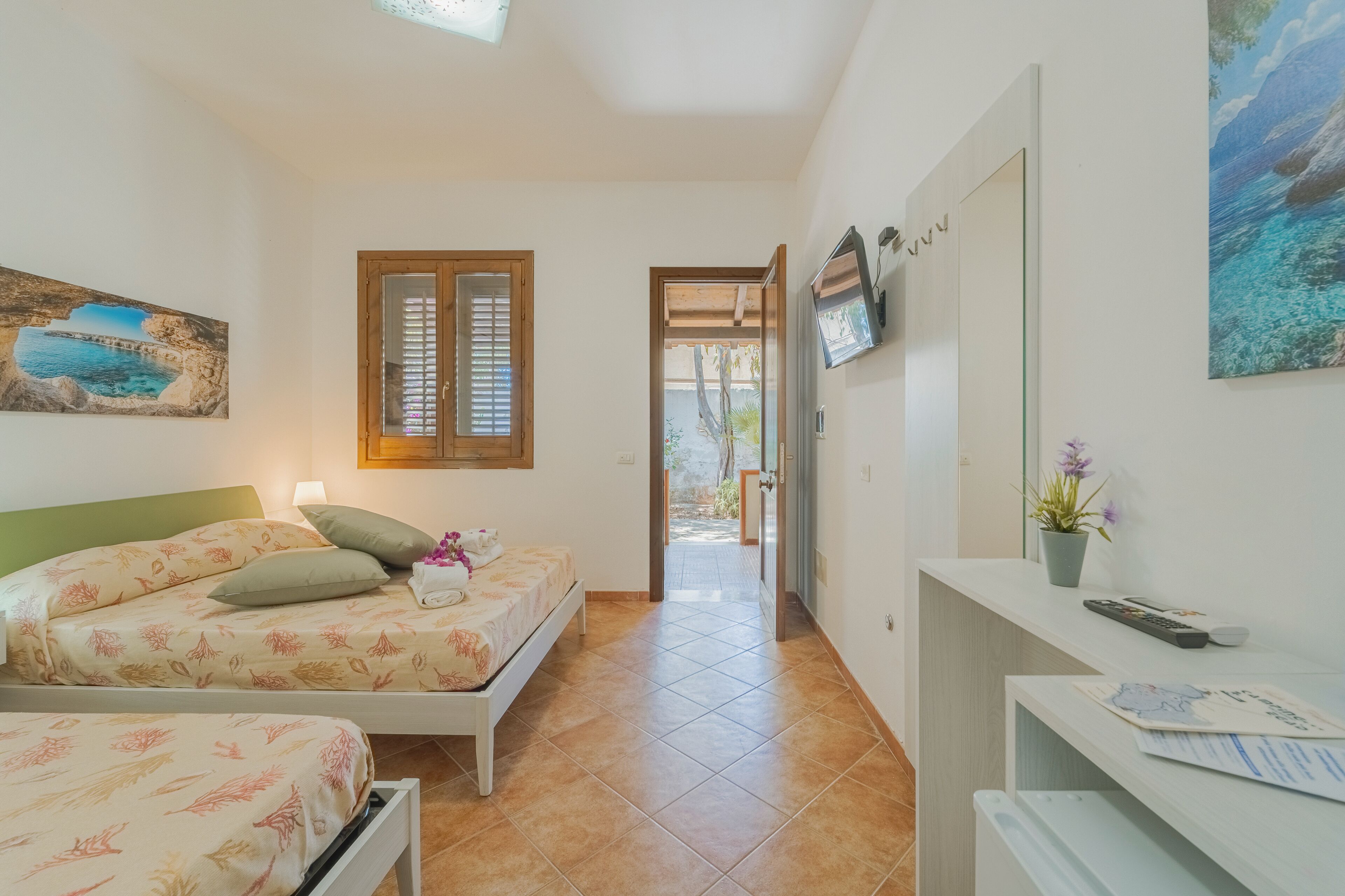 A bedroom with two beds, a TV, and a desk with a plant.