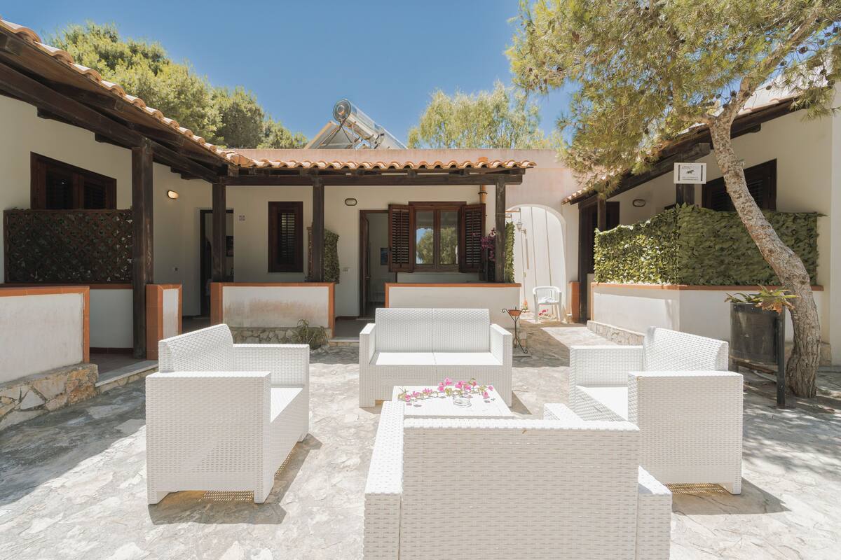 A covered outdoor seating area with white wicker furniture and a stone floor.