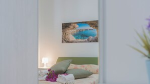 Un dormitorio con cama, almohadas, lámpara y un cuadro de una escena costera.