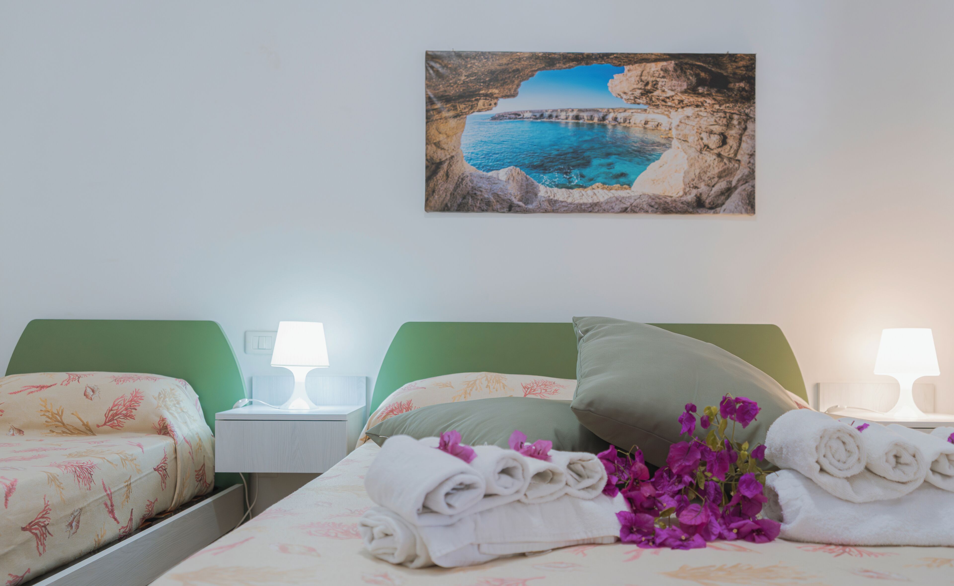 Una camera d'albergo con due letti, un quadro che raffigura una scena costiera e asciugamani sul letto.