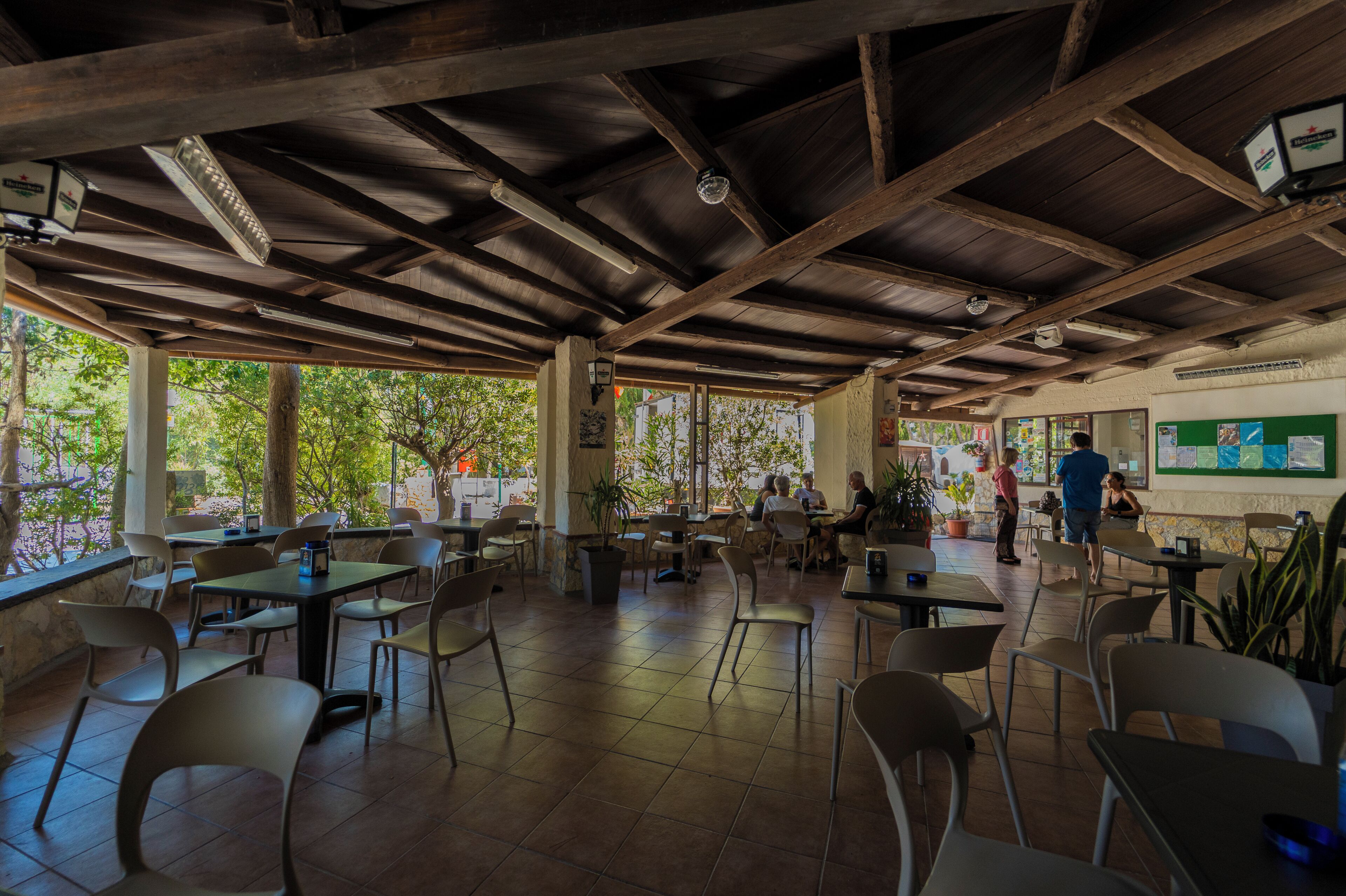 An indoor dining area with wooden beams, tiled floors, and tables with chairs.