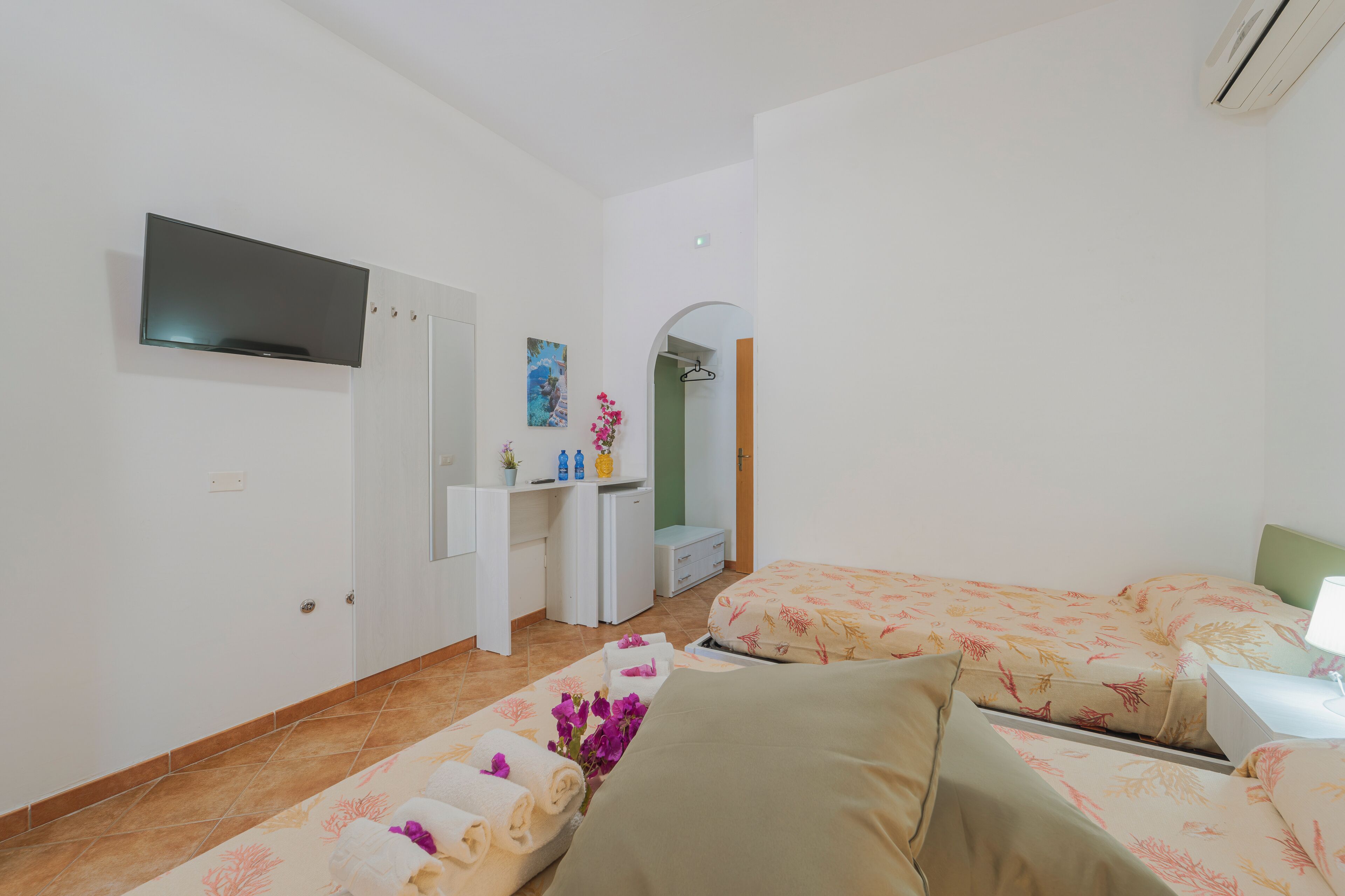 A hotel room with a TV, a desk with a mirror, a bed with floral bedding, and a small bathroom.