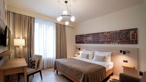 A hotel room with a bed, a desk, a chair, a lamp, and a large patterned artwork on the wall. - Mercure Belgrade Excelsior (Belgrade)