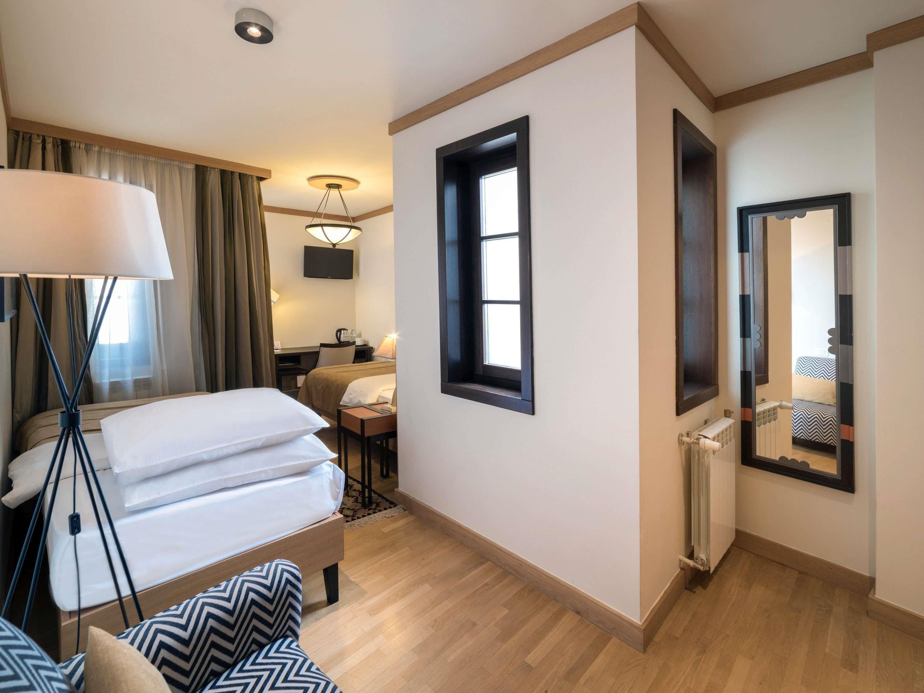 Et hotelværelse med seng, sengebord, lampe og udsigt til et andet værelse.