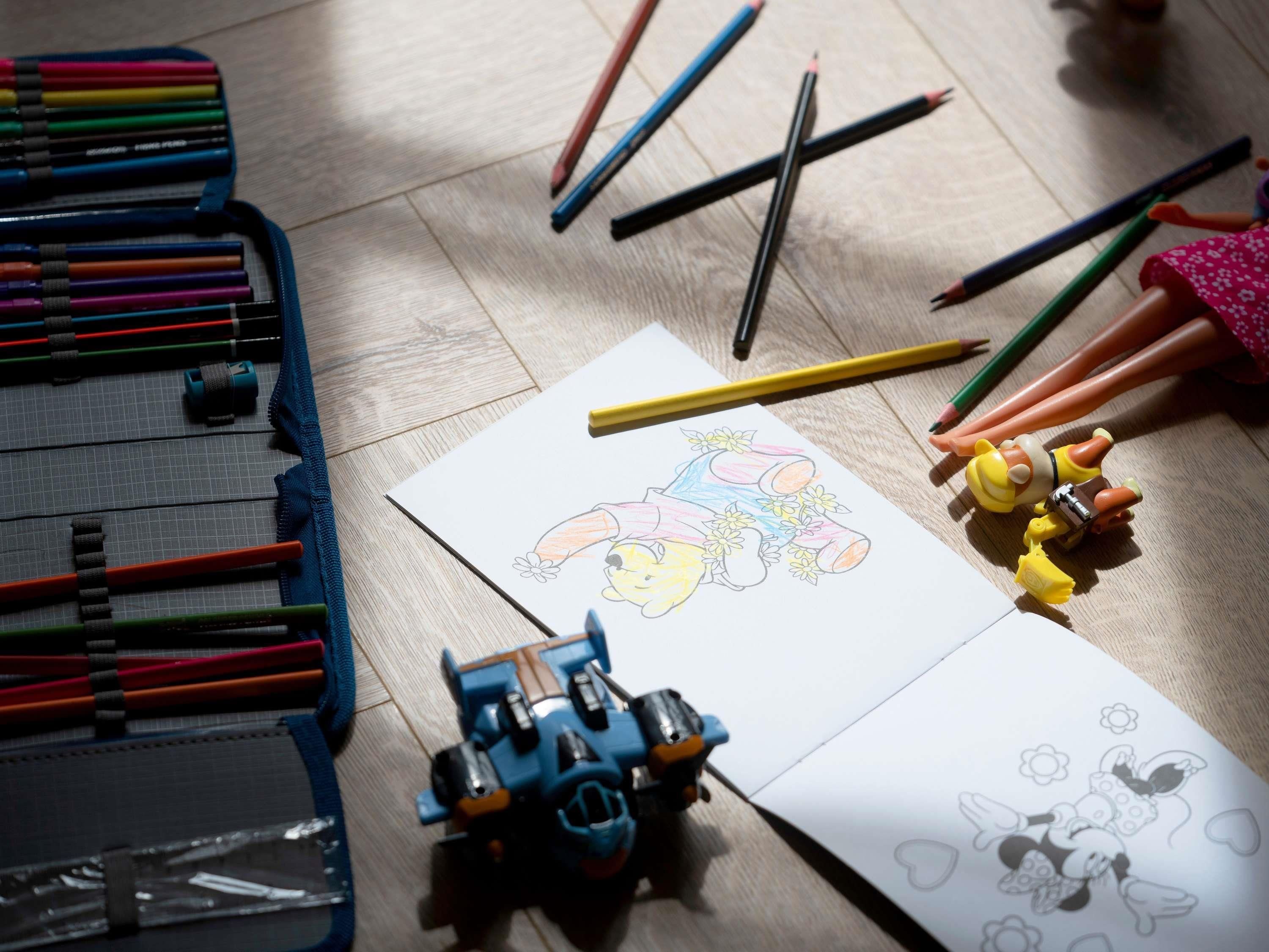 Papel de dibujo con un personaje de caricatura, lápices de colores y una figura de juguete.