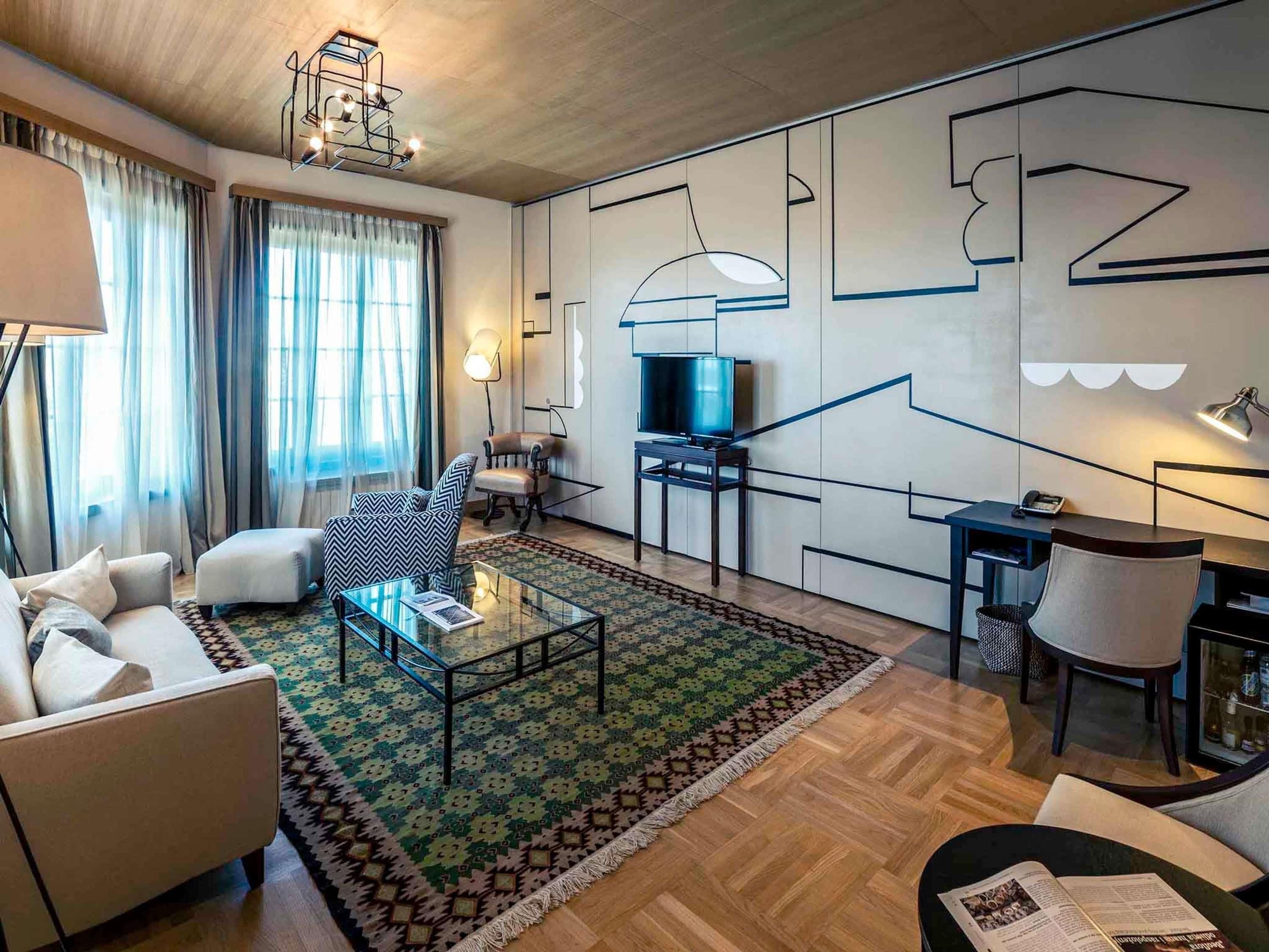 Una sala de estar moderna con sofá, sillón, mesa de centro, televisor y una alfombra estampada.