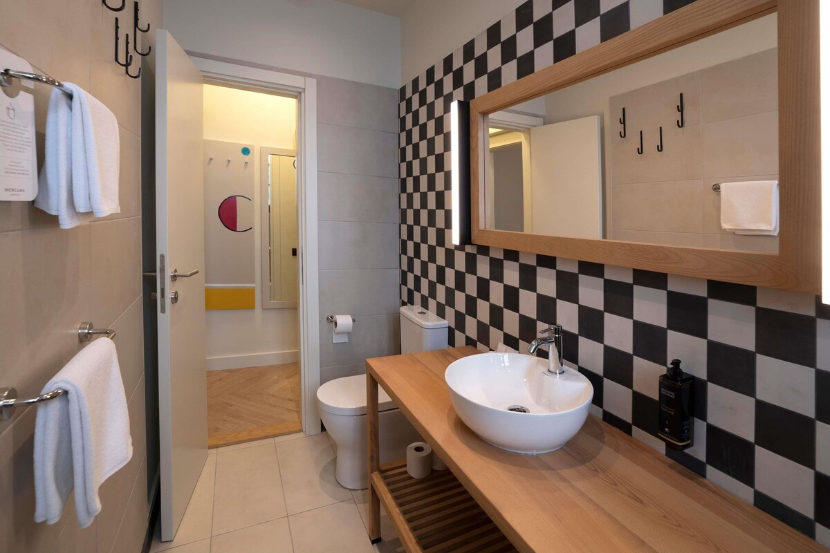 A modern bathroom with a checkered wall, a large mirror, a wooden vanity, and a toilet.