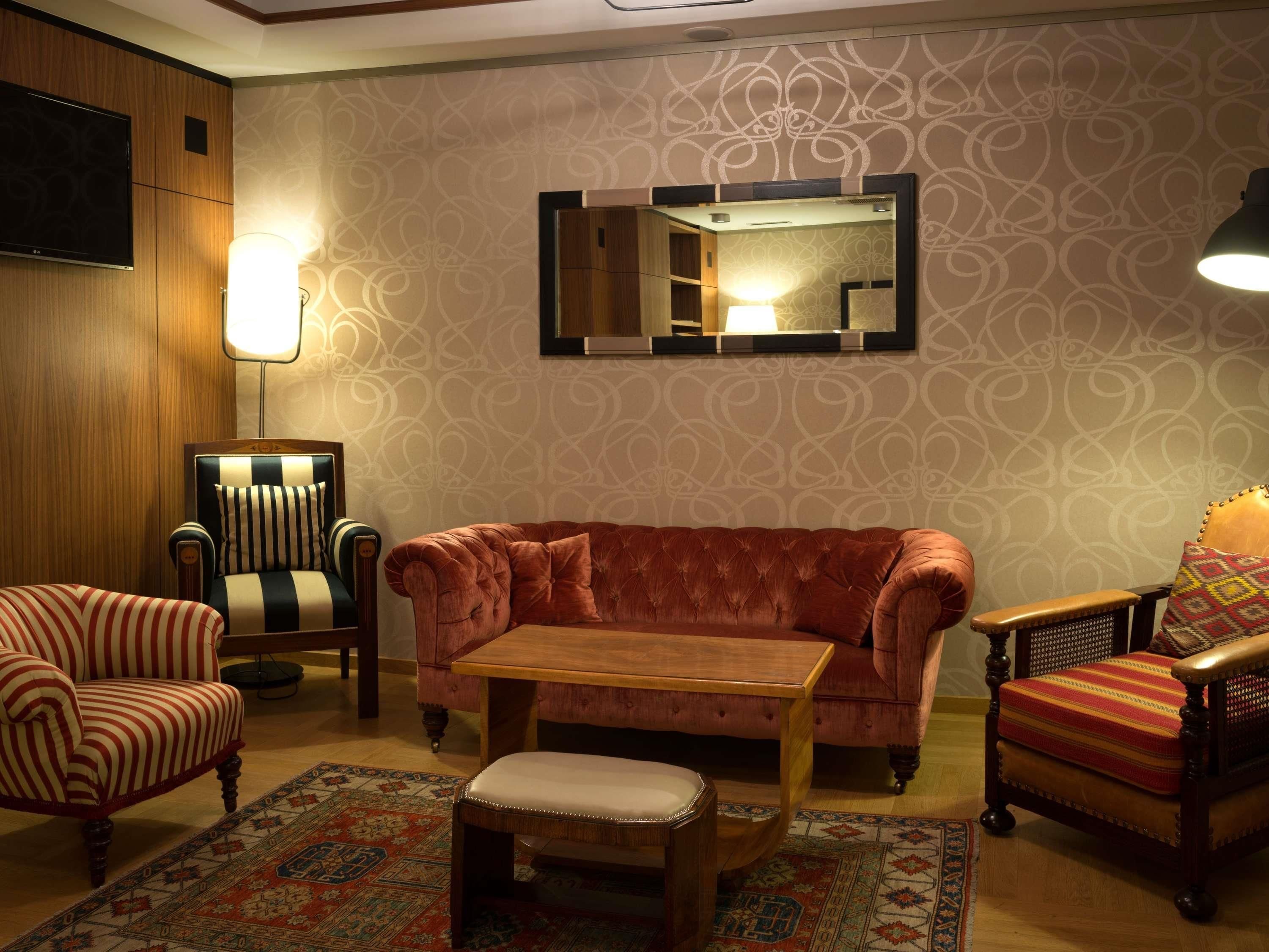 A room with a sofa, armchair, ottoman, and a table.