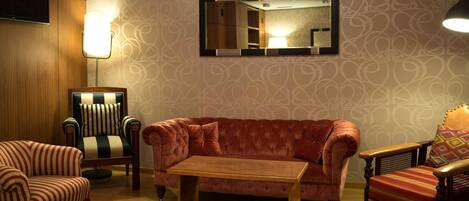 A room with a sofa, armchair, ottoman, and a table.