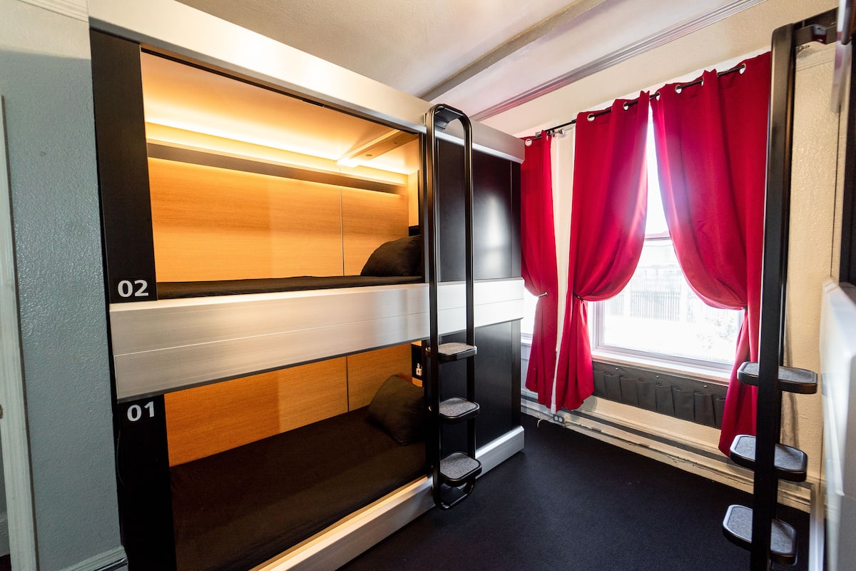 Un compartimento de tren con literas, una estantería y una ventana con cortinas rojas.