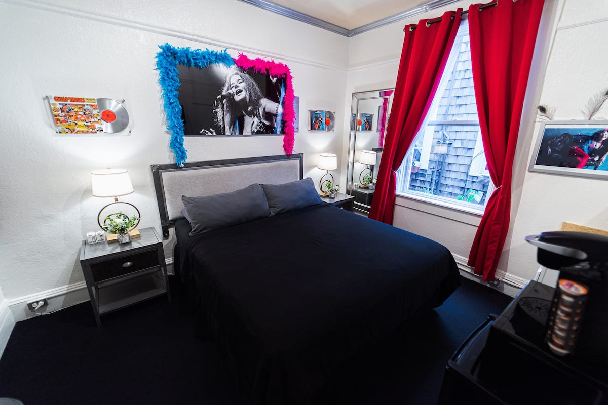 Un dormitorio con una cama, mesitas de noche, un espejo y una ventana con cortinas rojas.