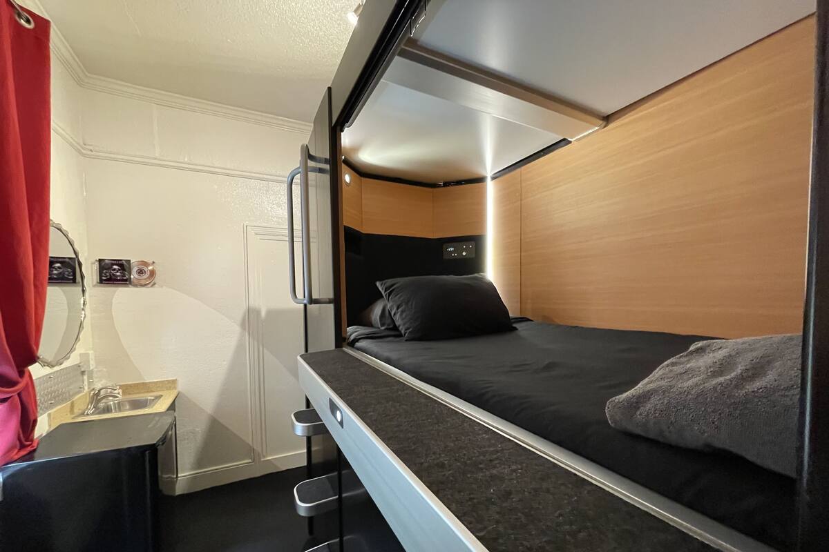 Habitación pequeña y bien iluminada con una litera, un escritorio con espejo y un lavabo.